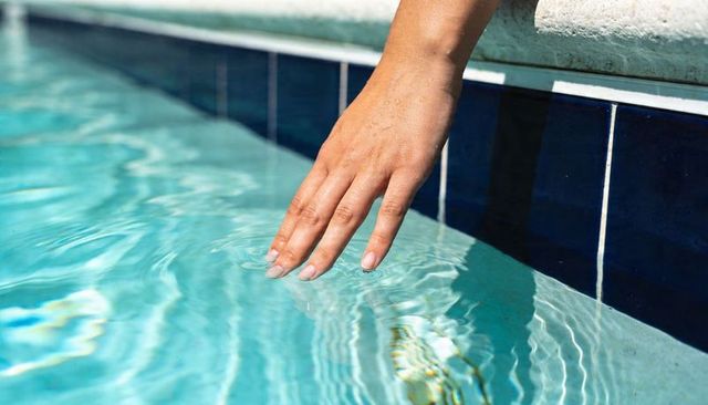 Hand skimming turquoise pool water creating ripples and sunlit caustic reflections