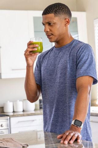 African american man drinking green juice in bright kitchen during healthy morning routine