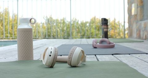 Beige wireless headphones resting on yoga mat by pool for outdoor fitness and wellness
