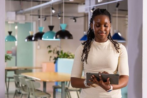 African american woman using tablet in modern pastel coworking space with teal lights