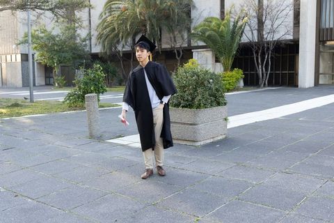 Asian graduate celebrating with diploma in modern university courtyard