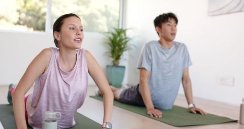 Couple practicing yoga at home doing cobra stretch on mats for wellness