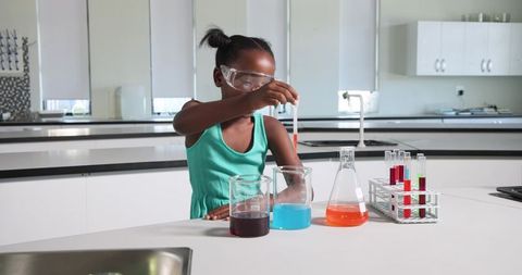 African american teen wearing goggles performing colorful chemistry experiment in school laboratory