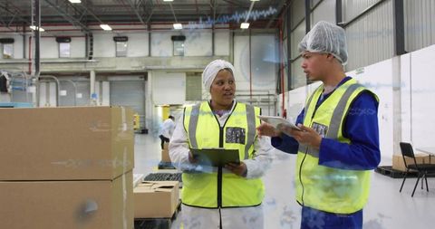 Warehouse team checking inventory with tablet and clipboard in distribution center, wearing vests