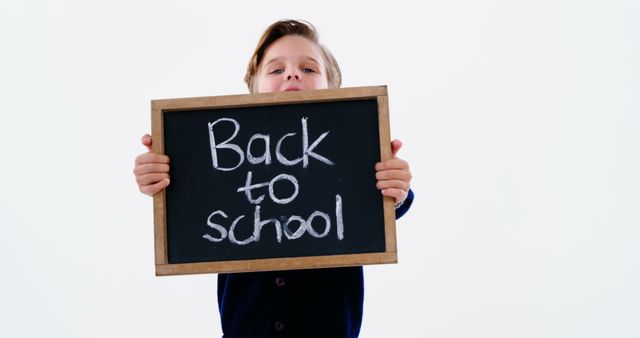 A young Caucasian boy holds a chalkboard with the words Back to School written on it, with copy space. His expression and the message on the board convey the theme of returning to education after a break.