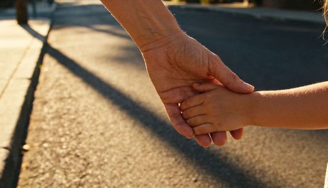 Holding parent and child hands on sunlit curb during golden hour conveying trust