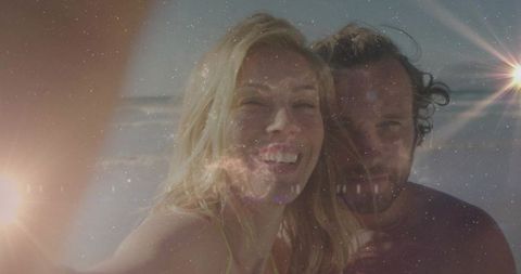 Couple enjoying sunny beachfront selfie with vibrant lens flare