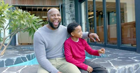 African american father and son laughing, pointing on patio pool edge, family bonding