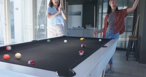 Friends cheering and clapping after winning pool game in sunlit modern home interior