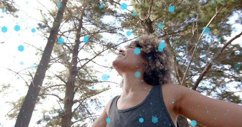 Curly-haired woman stretching arms toward sunlit forest canopy with cyan hexagon overlay