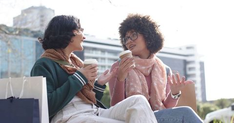 Diverse friends chatting and sipping coffee on urban park bench during casual city outing