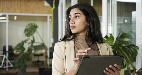 Indian businesswoman using tablet in modern coworking office with greenery and glass panels