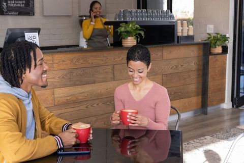 African american couple sharing coffee and smiling in cozy modern cafe with red mugs