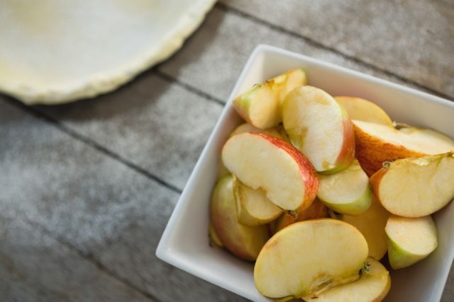 This image shows fresh apple slices in a white bowl placed on a rustic wooden table. Ideal for use in food blogs, healthy eating articles, recipe websites, or advertisements promoting fresh produce and healthy snacks.