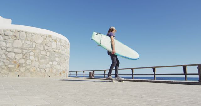 Image of caucasian man with dreadlocks skateboarding carrying surfboard on sunny beach promenade. Freedom, sport, hobbies and healthy active lifestyle concept digitally generated image.