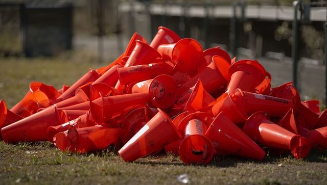 Pile of bright orange traffic cones on grassy ground showing littered safety markers
