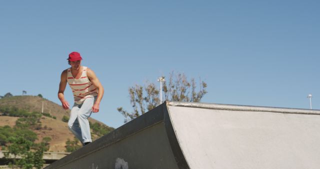 This image shows a young man skating at an outdoor skate park on a sunny day. He is wearing a red cap and casual summer clothes. This photo captures the essence of outdoor activity and youthful energy, making it suitable for use in advertisements for sports gear, summer activities, and healthy lifestyle campaigns.