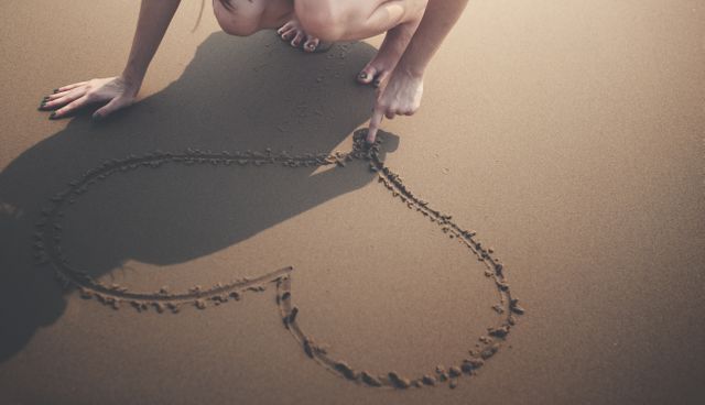 Person is drawing a heart shape in the sand on a beach, symbolizing love, romance, and intimate moments. Perfect for themes around relationships, romantic getaways, summer vacations, or creative artistic expressions.