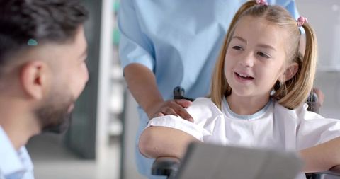 Smiling girl in wheelchair talking with doctor and caregiver in pediatric clinic