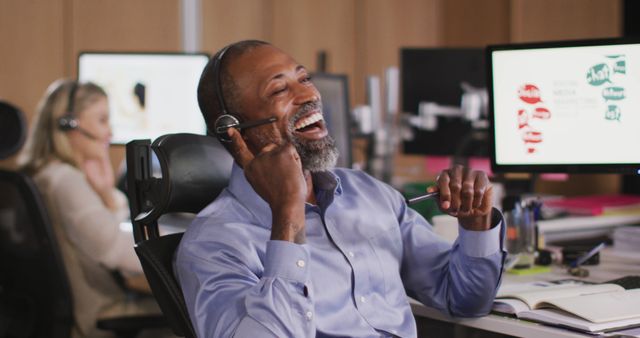 African American man is laughing while working in a modern office. Great for use in articles, advertisements, or websites focused on customer service, work environments, professional settings, and office culture. Suitable for illustrating positive workplace experiences, teamwork, or customer satisfaction.