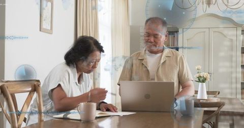 Senior couple reviewing finances at home with laptop and paperwork, planning together