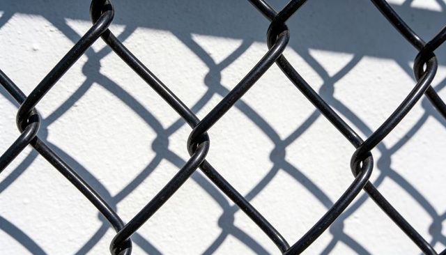 Black chain-link fence casting diamond mesh shadows on white stucco wall
