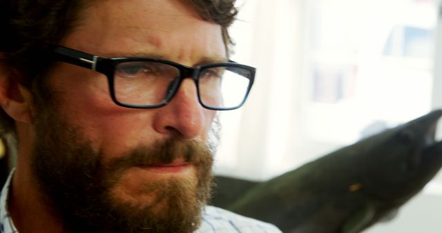A middle-aged Caucasian man with a beard and glasses appears pensive or focused, with copy space. His expression suggests deep thought or concern, set against a blurred background that includes a fish model.