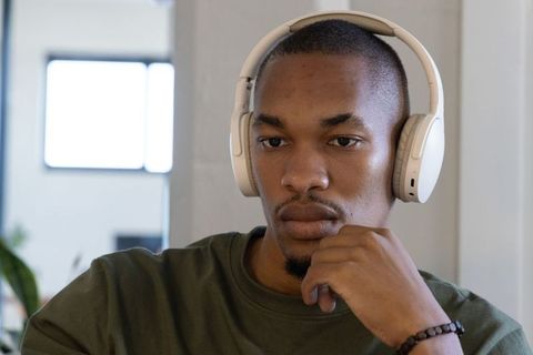 African american man wearing white headphones and olive shirt looking contemplative at home