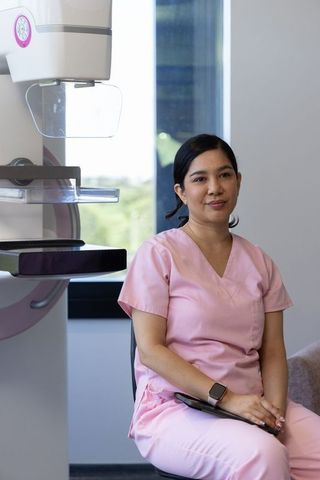 Female radiology technologist sitting by mammography unit wearing pink scrubs holding tablet