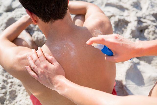 High angle view of woman applying spray on man back at beach during sunny day