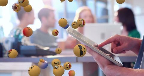 Person Using Tablet with Floating Emojis in Modern Office