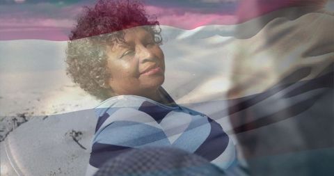 African american woman relaxing on sandy beach with flag double exposure
