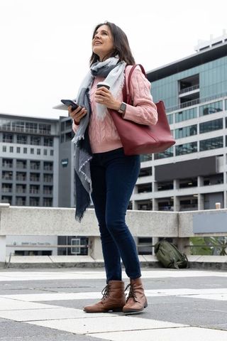 Urban commuter woman holding coffee and smartphone wearing pink sweater with red tote