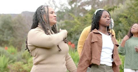 Multigenerational diverse family holding hands in garden, teenage girl wearing pale green headband
