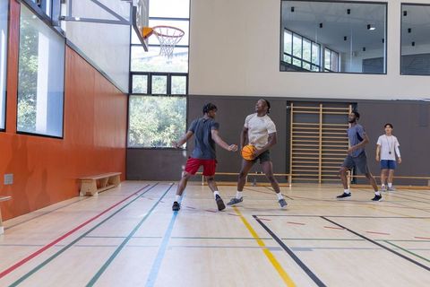Young men dribbling, defending and practicing shots in daylight indoor basketball training