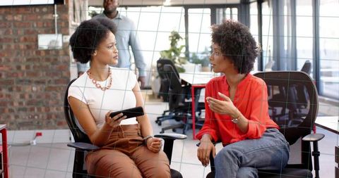 Two women collaborating in modern office discussing project holding tablet
