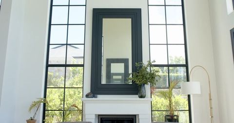 Sunlit living room with white fireplace mantel, black-framed mirror and greenery