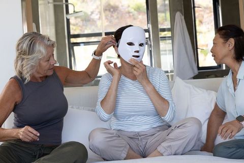 Mature women trying led light therapy facial mask together during relaxed at-home skincare