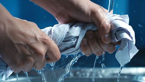 Hands wringing wet white fabric under running water squeezing dripping cloth for laundry