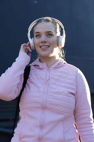 Young Woman Listening to Music with Headphones Wearing Pink Jacket in Sunlit Urban Portrait