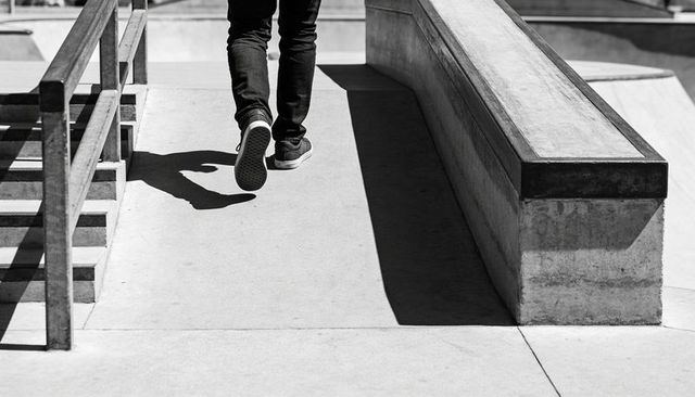 Urban Skatepark Walk: Lower Body in Jeans and Sneakers Passing Handrail and Grind Ledge