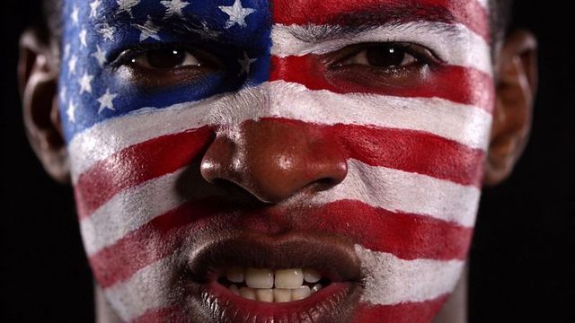 Black man wearing american flag face paint, intense close-up portrait with dramatic low-key lighting