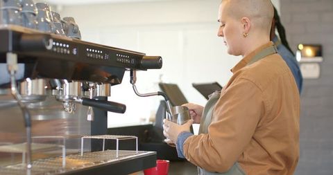 Multicultural barista steaming milk with espresso machine at busy cafe counter preparing latte