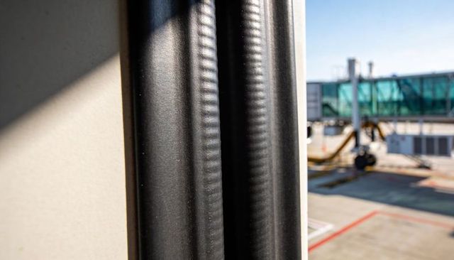 Sunlit vertical aircraft window seal close-up with jet bridge and tarmac background