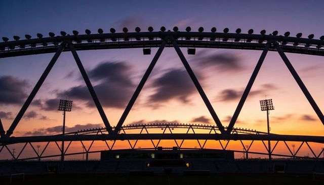 Stadium steel arches silhouette at sunset featuring triangular truss geometry and lights