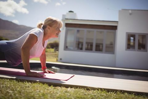 Senior Woman Exercising on Yoga Mat Outdoors Beside Pool