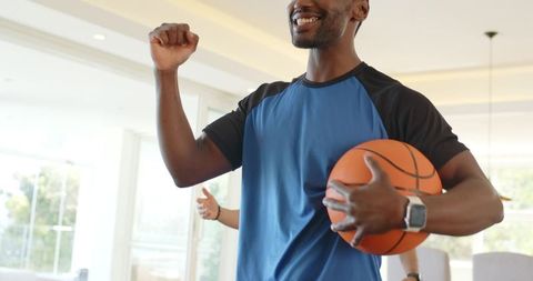 Black man celebrating victory with basketball at home wearing sports jersey and smartwatch