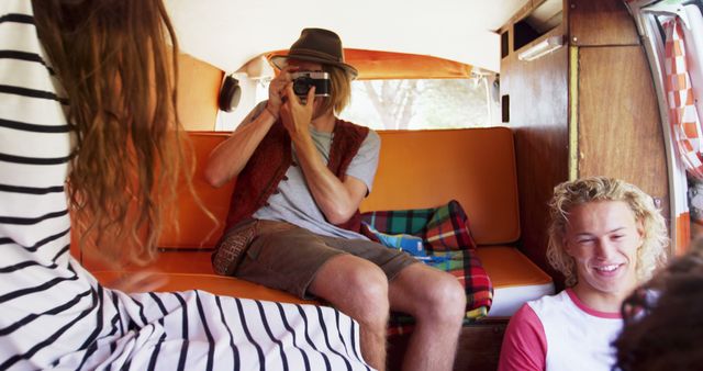 Young Caucasian man captures a moment inside a vintage van. Friends enjoy a road trip, creating memories in a cozy, retro setting.
