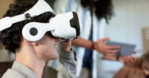 Young man testing white VR headset while diverse coworkers collaborating with tablet