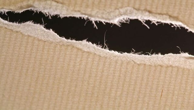 Tearing beige corrugated cardboard revealing fibrous torn edges and dark void